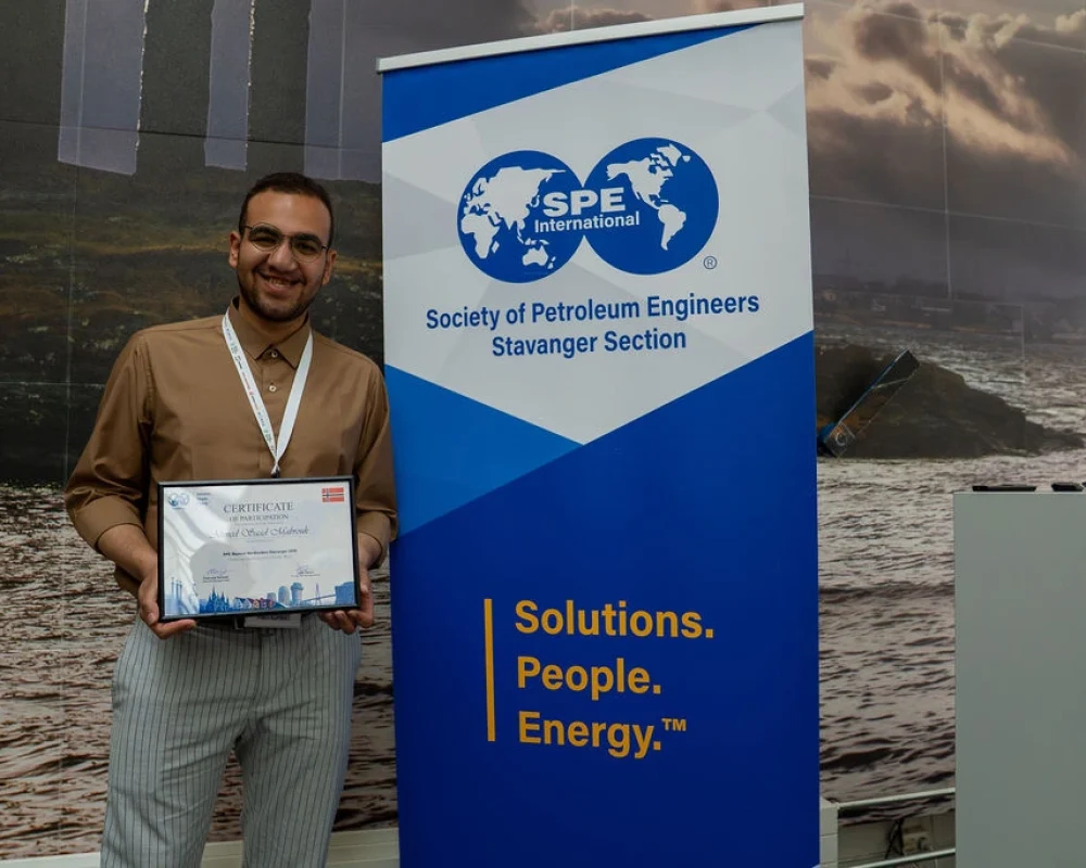Ahmed Saad smiles while holding a certificate of participation beside a Society of Petroleum Engineers (SPE) International Stavanger Section banner at an event in Stavanger.